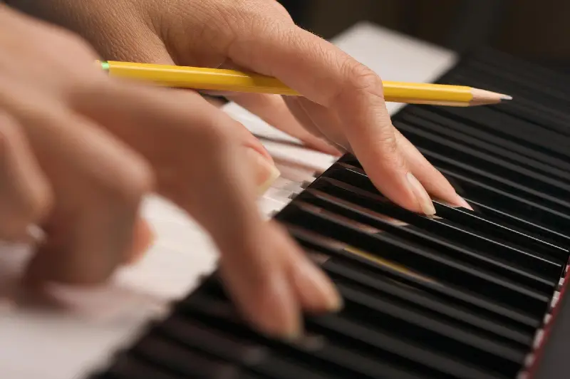 Deux mains sur les touches d'un clavier, un crayon tenu entre les doigts de la main droite