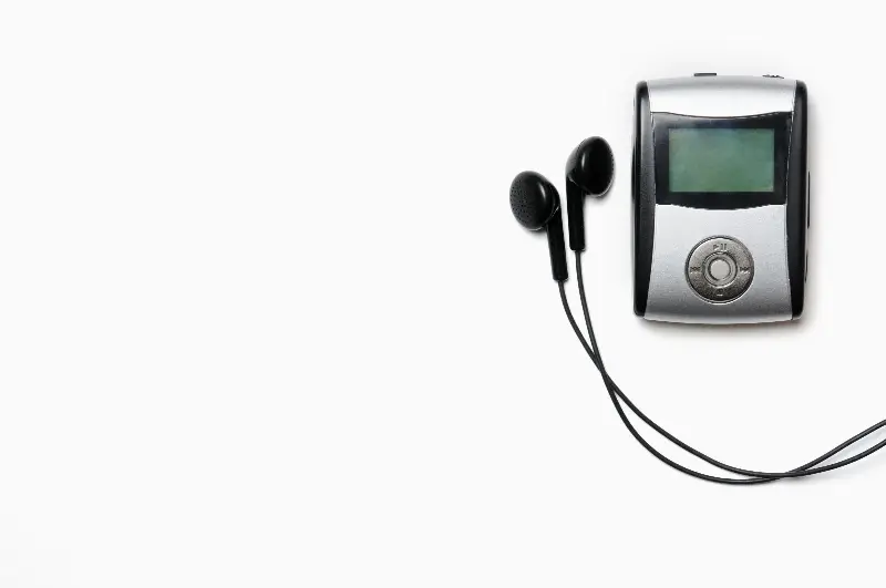 Ancien baladeur MP3 argenté à petit écran, avec ses écouteurs, sur fond blanc