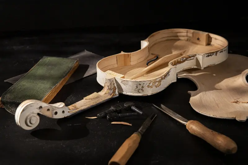 Violon démonté sur un établi : caisse sans sa table, table posée à côté, manche, chevilles et deux outils de luthier
