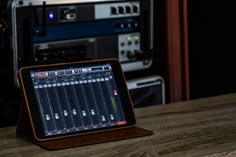 Application de mixage ouverte sur une tablette, avec ses faders, devant un rack d'appareils audio