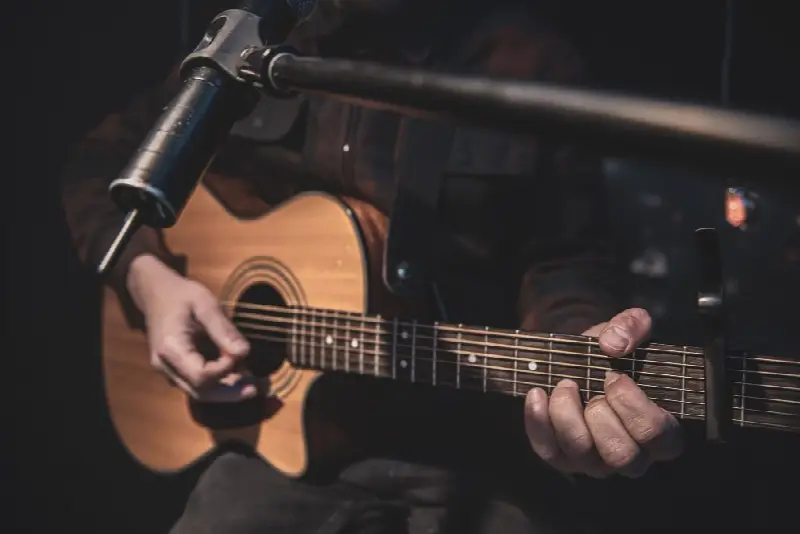 Guitariste jouant une guitare folk à pan coupé devant un micro sur perche, un capodastre sur le manche