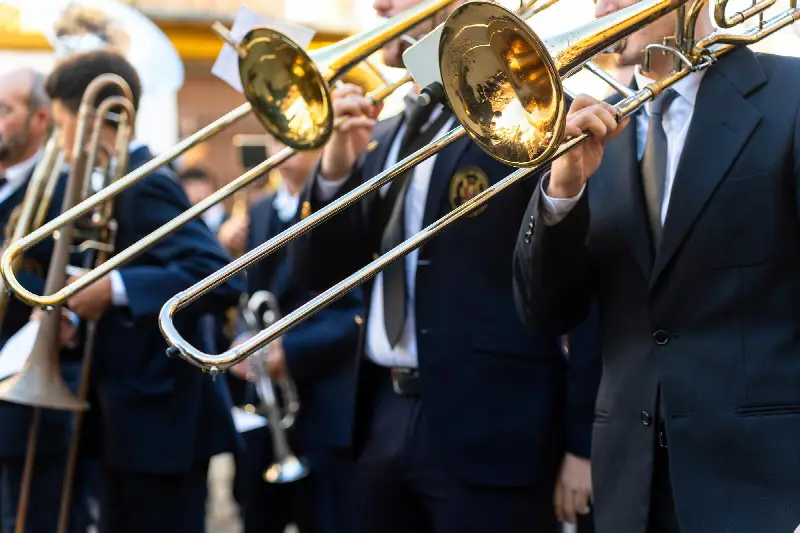 Trombonistes et trompettiste d'une fanfare en costume sombre jouant en plein air