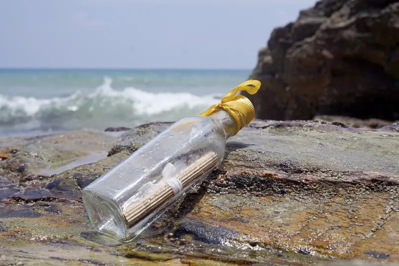Bouteille de verre échouée sur des rochers, entre deux vagues