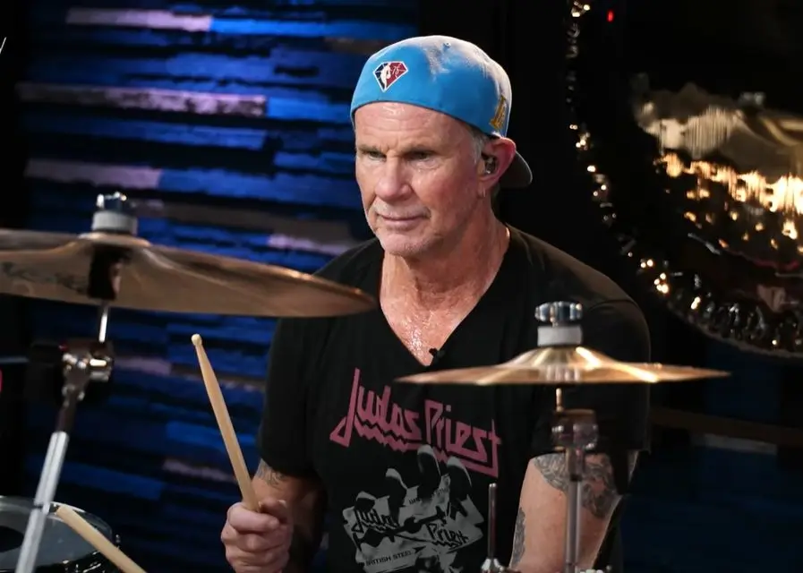 Chad Smith à la batterie, casquette bleue à l'envers et t-shirt Judas Priest, baguette en main
