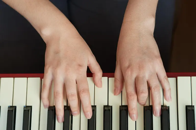 Deux mains posées à plat sur le clavier d'un piano de scène rouge, vues du dessus