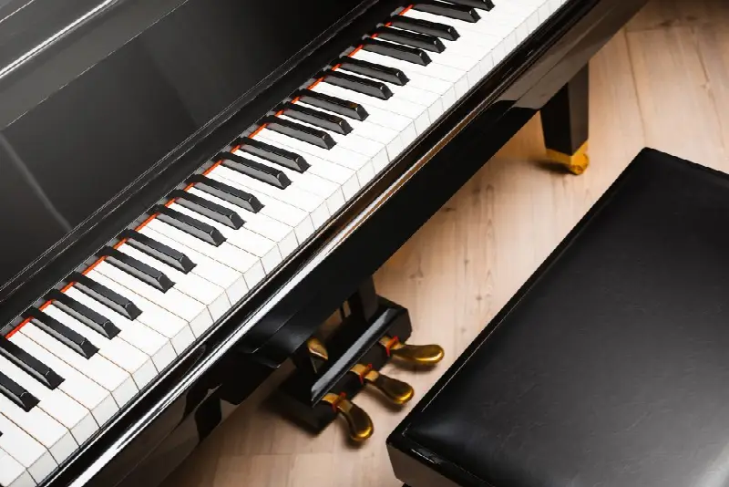 Clavier d'un piano noir vu d'en haut, avec ses trois pédales dorées et une banquette en cuir
