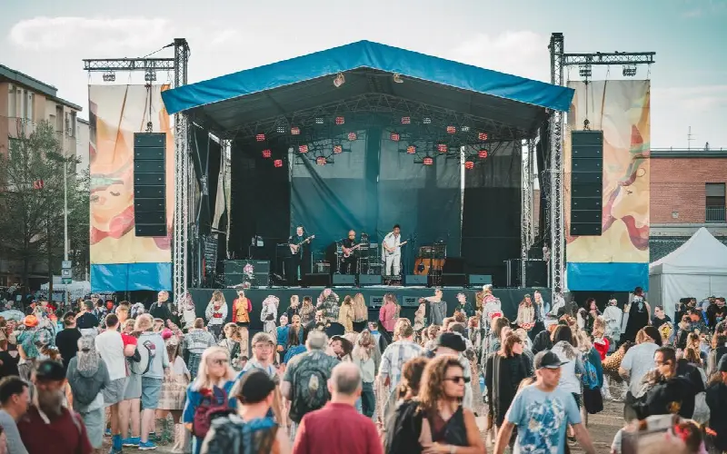 Concert en plein air : un groupe joue sur une scène couverte devant une foule debout, entre des immeubles