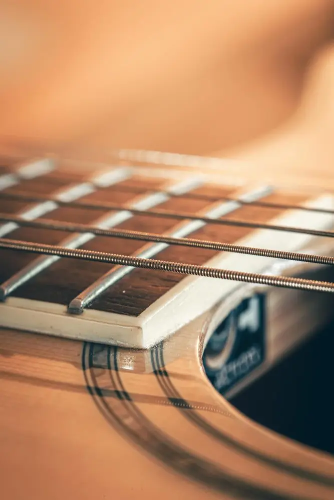 Gros plan sur les cordes filées d'une guitare folk au-dessus de la touche et du bord de la rosace