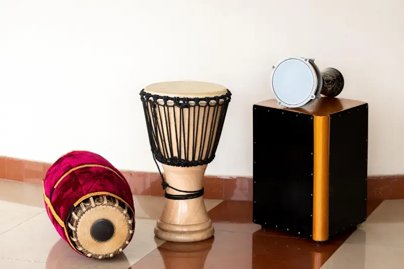 Darbouka en métal posée sur un cajón, à côté d'un djembé et d'un mridangam