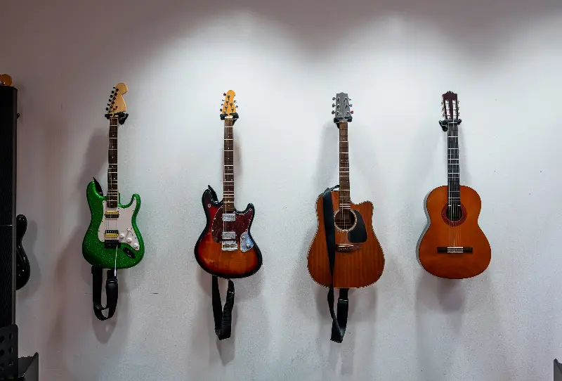 Deux guitares électriques, une folk et une classique suspendues à un mur blanc