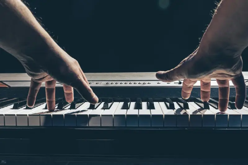 Deux mains posées sur le clavier d’un piano numérique, vues de face sur fond noir
