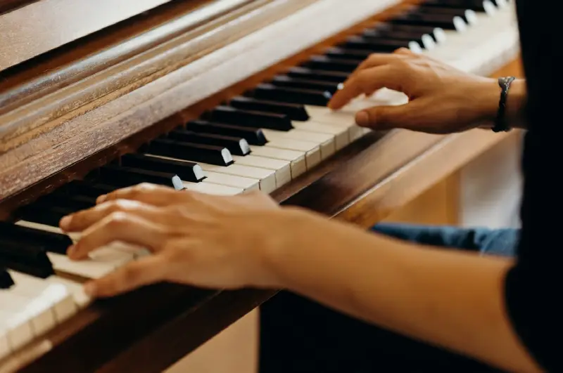 Deux mains sur le clavier d'un piano droit en bois, la main gauche dans le grave