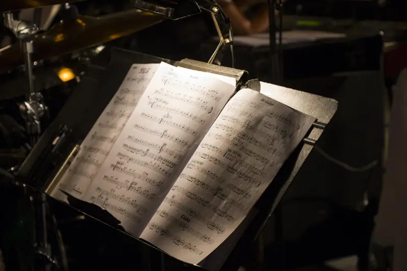Partition sur un pupitre éclairé, à côté des cymbales d'une batterie, sur scène