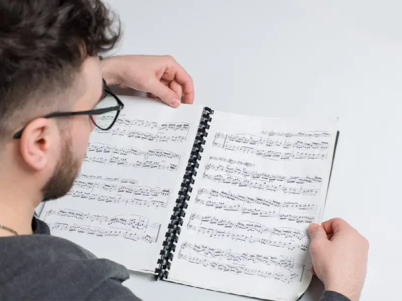 Homme à lunettes qui feuillette une partition de piano reliée par une spirale