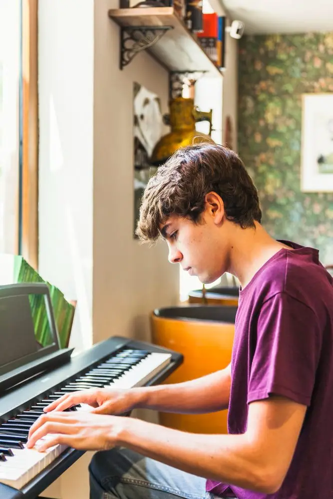 Adolescent en t-shirt violet qui joue d'un piano numérique près d'une fenêtre