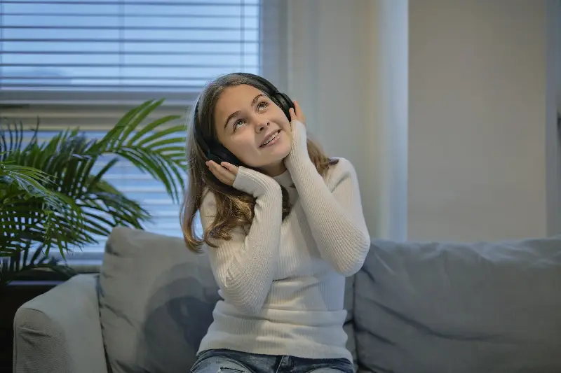 Fillette assise sur un canapé, les mains sur son casque, qui écoute de la musique
