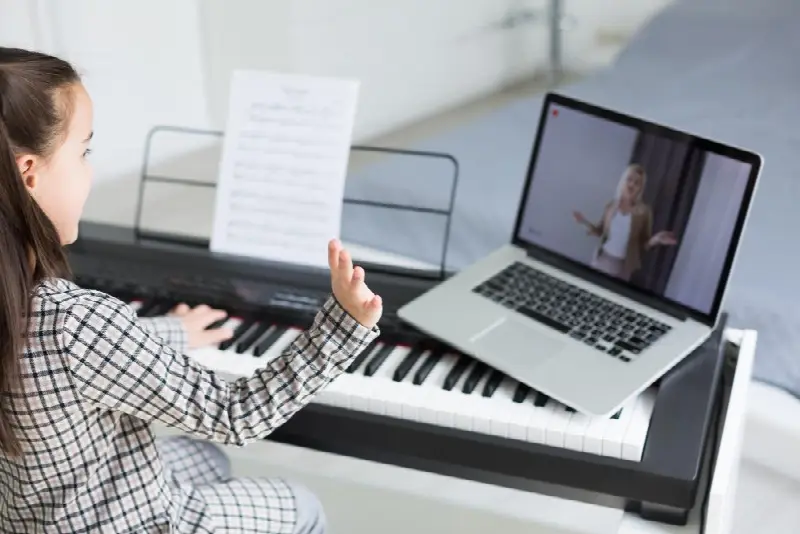 Fillette au clavier numérique qui suit un cours de piano en vidéo sur un ordinateur portable