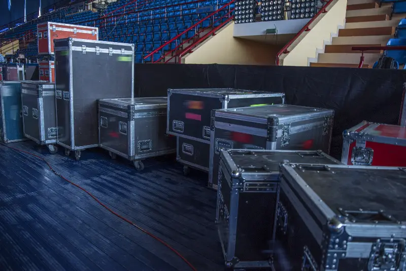 Flight-cases de matériel de tournée alignés au pied des gradins vides d’une salle de concert
