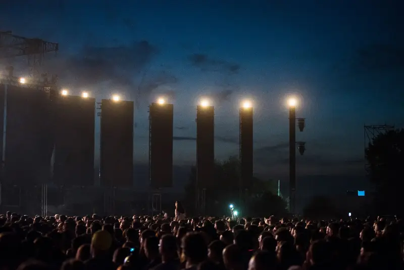 Foule d'un festival en plein air à la tombée de la nuit, face aux structures et projecteurs de la scène