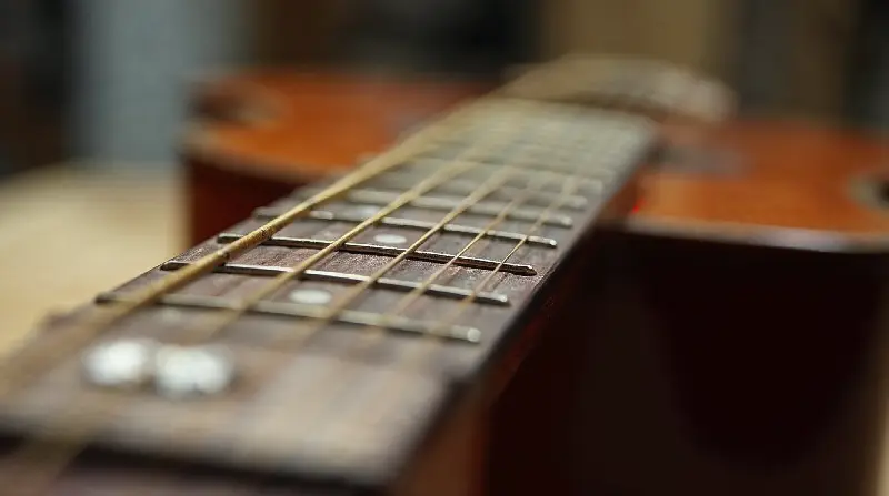 Gros plan sur le bord d'une touche de guitare folk et l'extrémité des frettes, vus de près