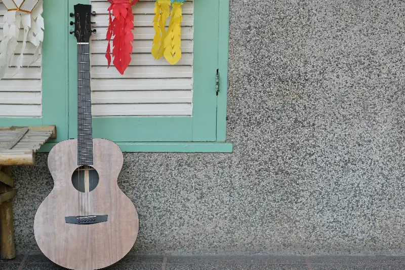 Guitare acoustique posée contre un mur, sous une fenêtre à persiennes
