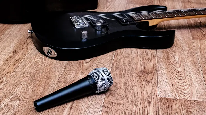 Guitare électrique noire posée sur un parquet, un micro dynamique couché à côté
