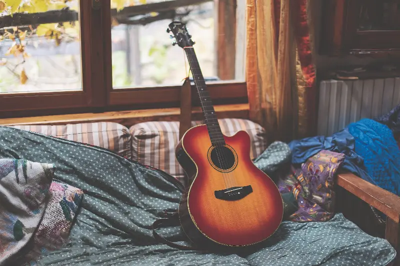 Guitare folk électro-acoustique sunburst posée sur un canapé près d'une fenêtre