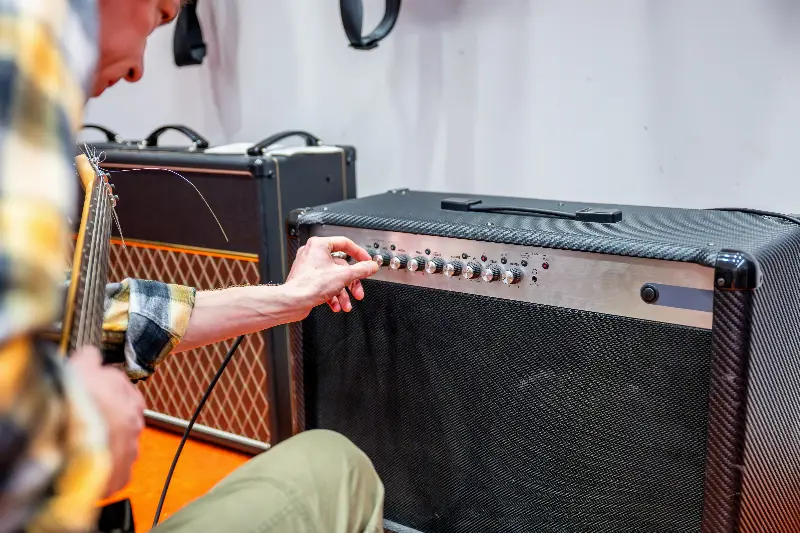 Guitariste réglant les boutons de son ampli, guitare électrique en main