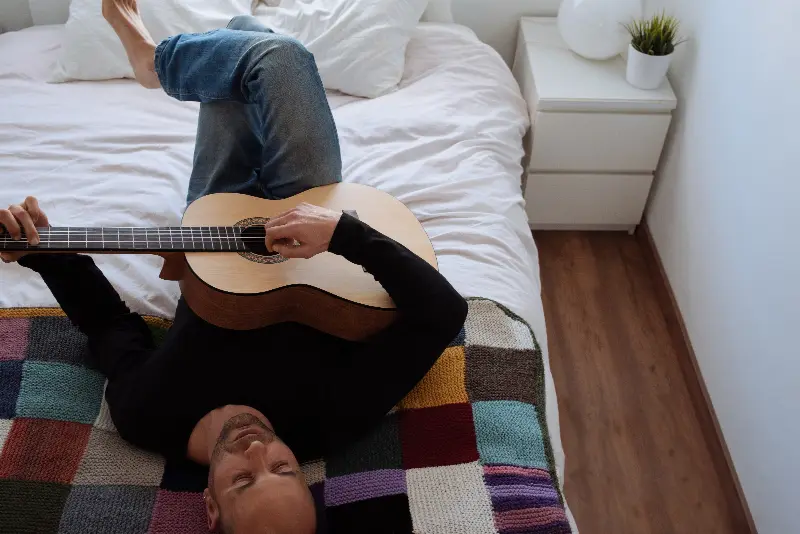 Homme allongé sur un lit, jouant d'une guitare classique posée sur son ventre