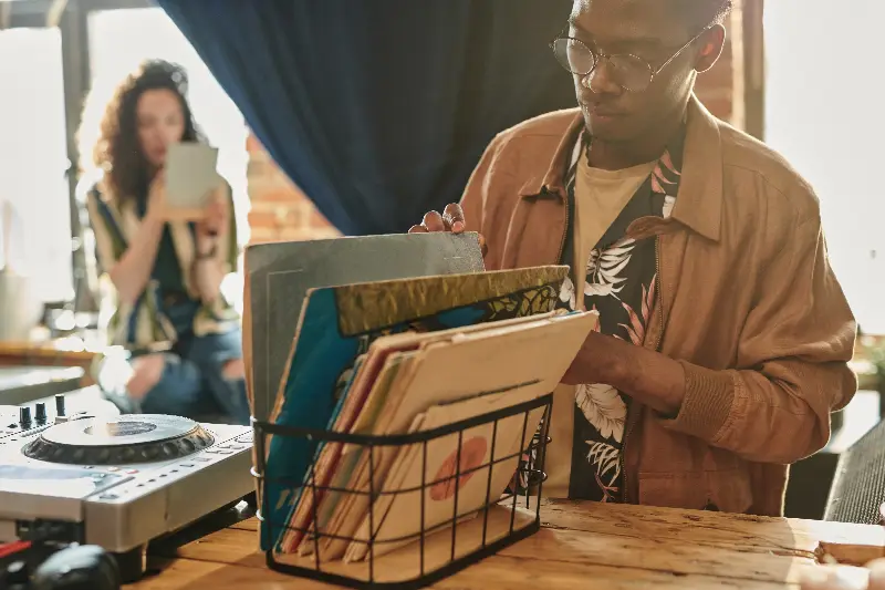 Homme qui feuillette des pochettes de disques vinyle rangées dans un panier, une platine de DJ au premier plan