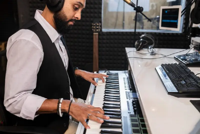 Musicien au casque jouant sur un clavier MIDI dans un studio aux murs couverts de mousse acoustique