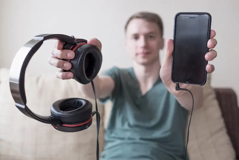 Jeune homme assis sur un canapé tendant un casque audio et un smartphone branché