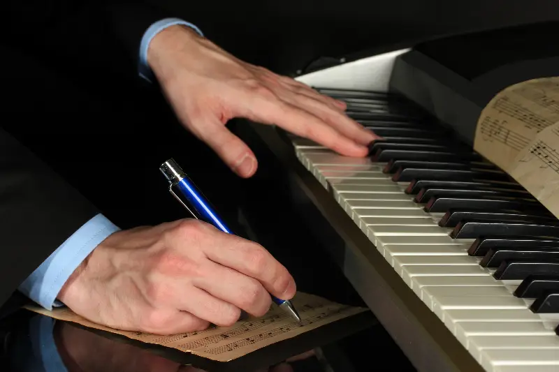Main d'un pianiste notant des notes au stylo sur une partition, l'autre main posée sur le clavier