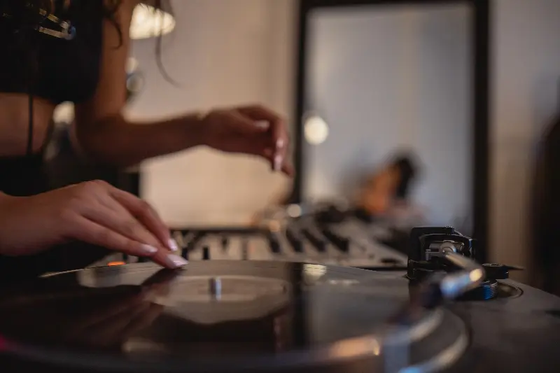 Main d'une DJ posée sur un disque vinyle, table de mixage floue à l'arrière-plan