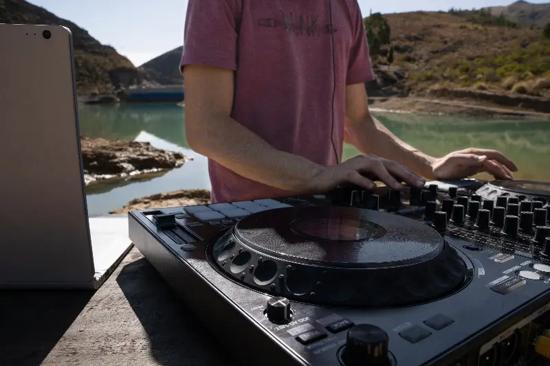 Mains d'un DJ sur un contrôleur de mixage installé au bord d'un lac de montagne