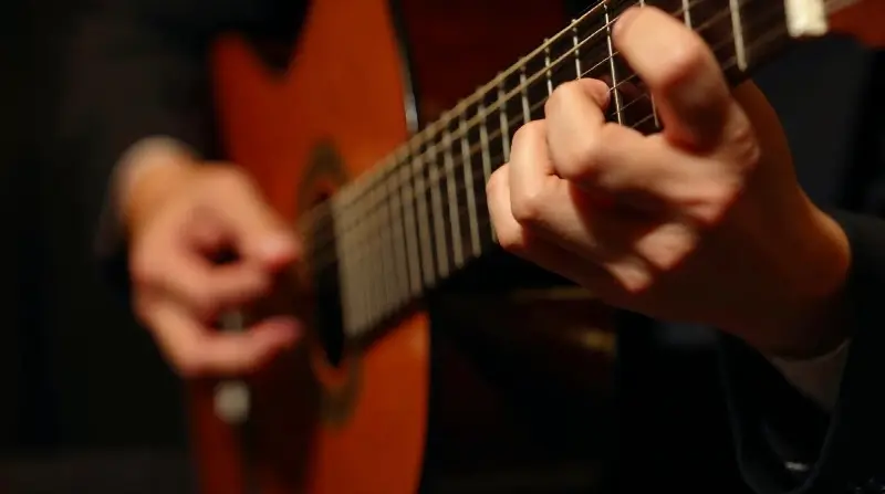 Mains d'un guitariste sur une guitare à cordes nylon : la main gauche forme un accord sur le manche, la droite gratte les cordes