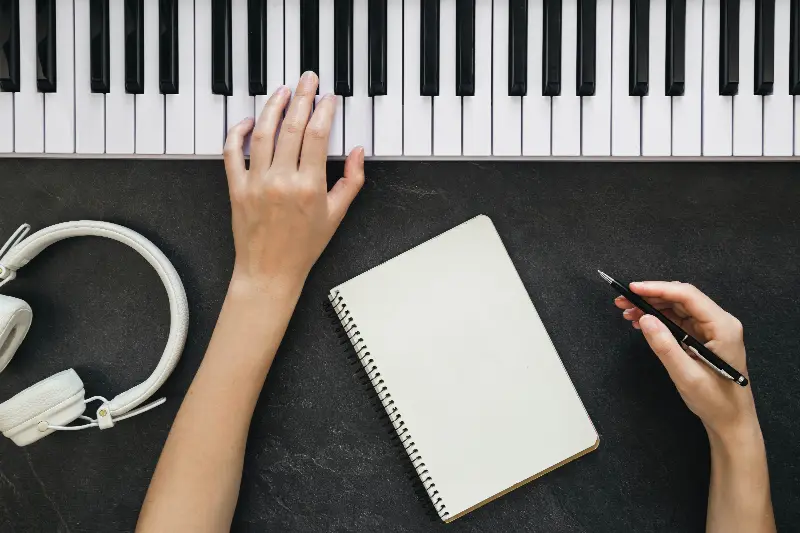 Mains posées sur un clavier numérique, à côté d'un carnet à spirale et d'un casque blanc
