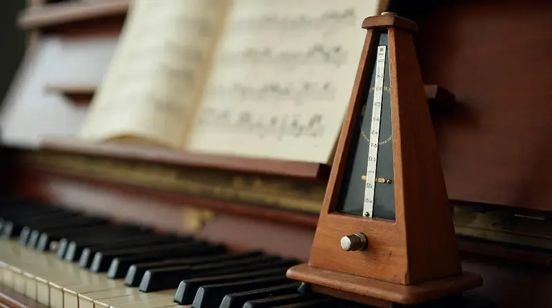 Métronome mécanique en bois posé sur le clavier d'un piano, devant une partition ouverte