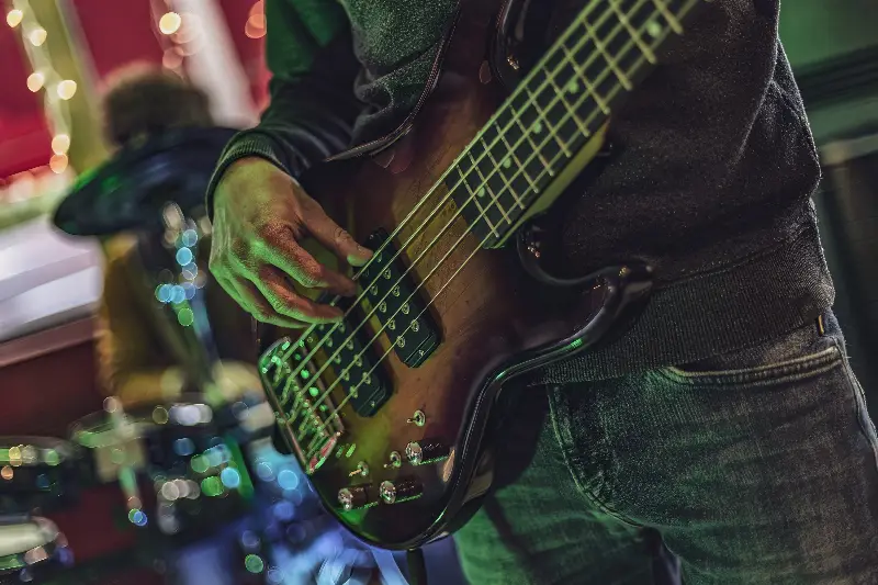 Musicien jouant d'une basse électrique à cinq cordes sur scène, dans une lumière verte