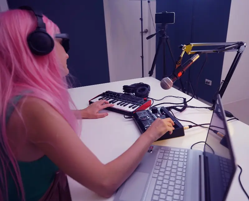 Musicienne au casque devant un clavier maître, une table de mixage et un micro sur bras