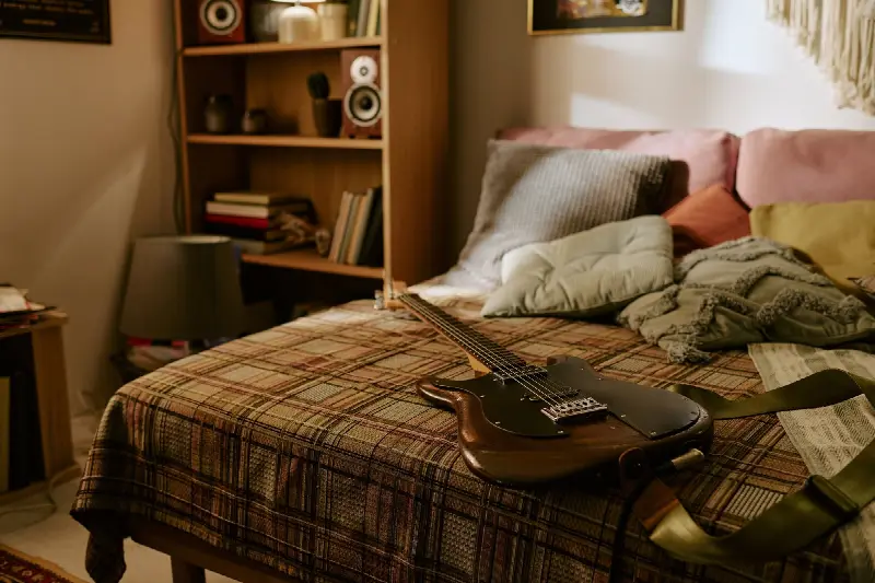 Une guitare électrique posée sur un lit à couverture écossaise, dans une chambre