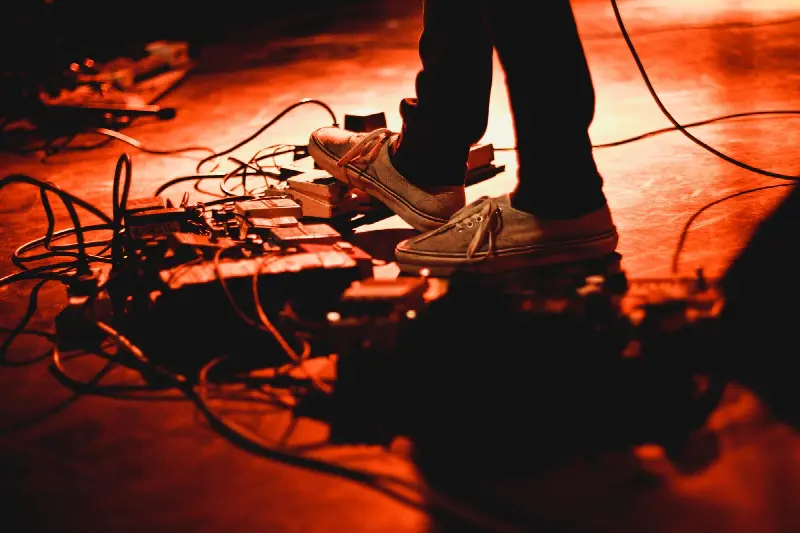 Pied d'un guitariste en baskets qui enfonce une pédale d'effet, sur une scène éclairée en rouge