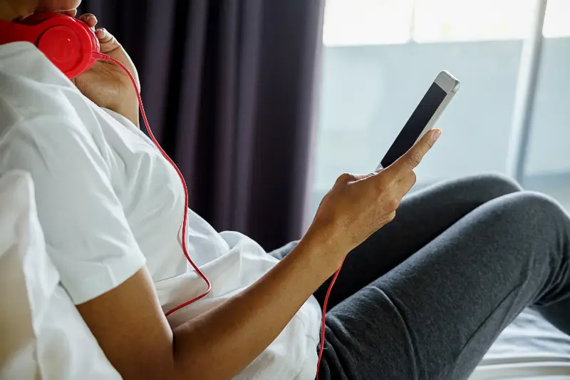 Personne assise, un casque filaire rouge autour du cou, qui regarde son smartphone