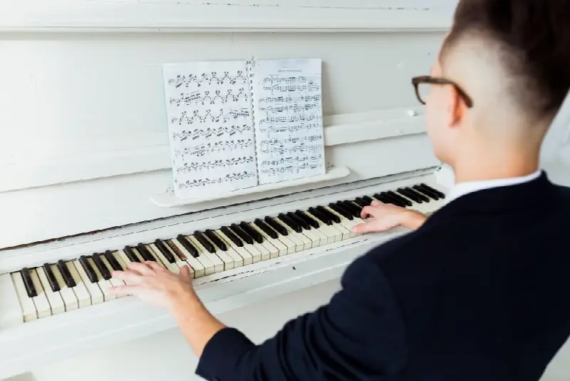 Pianiste de dos qui joue sur un piano droit blanc, une partition ouverte sur le pupitre