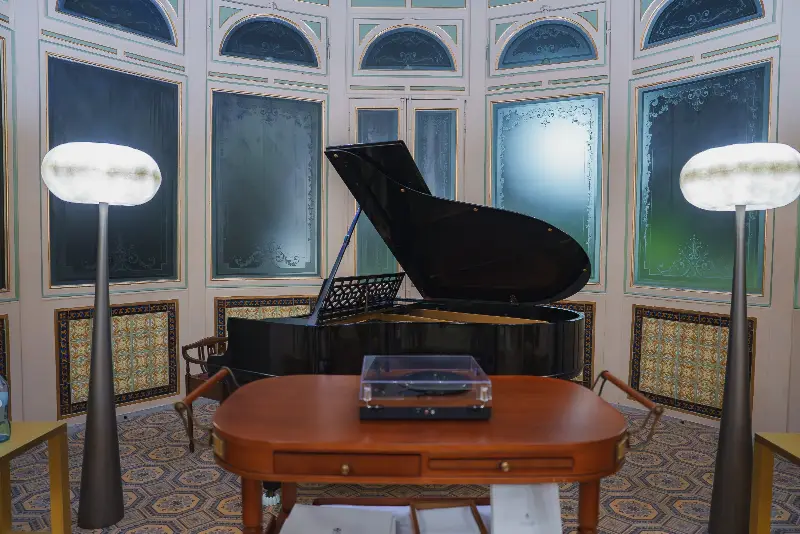 Piano à queue noir ouvert dans un salon aux boiseries peintes et aux vitres gravées