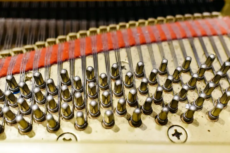 Rangées de chevilles d'accord en acier autour desquelles s'enroulent les cordes d'un piano, feutre rouge en arrière-plan