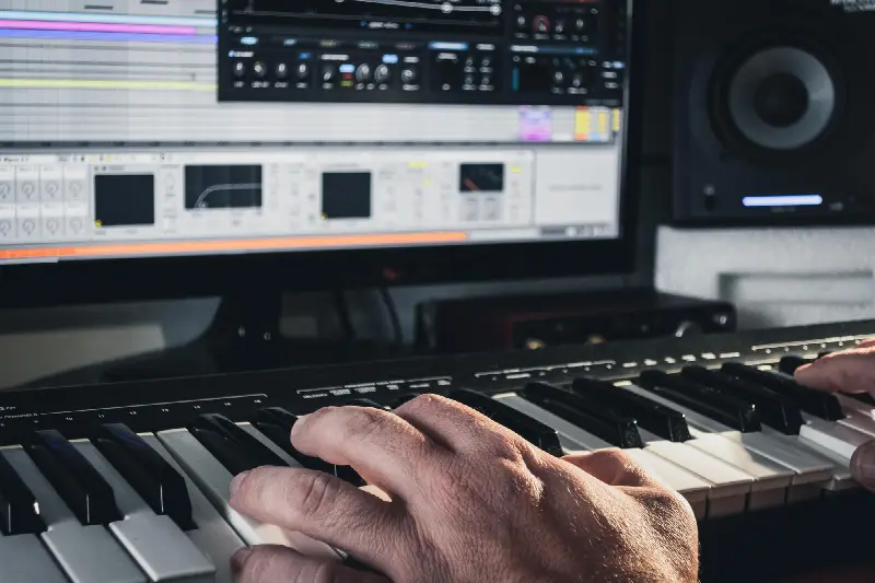 Mains sur un clavier maître MIDI, devant un écran de logiciel de musique et une enceinte de studio