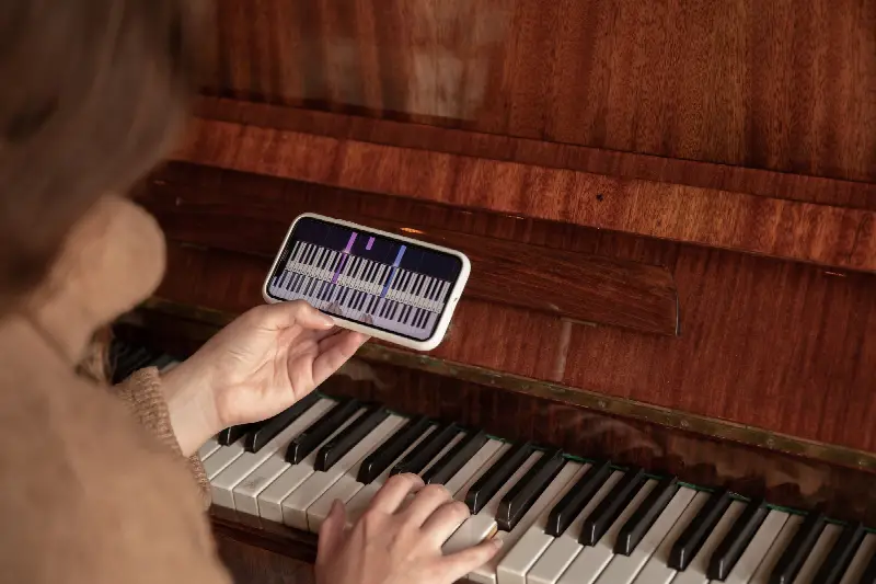 Pianiste qui tient son téléphone au-dessus du clavier d'un piano droit