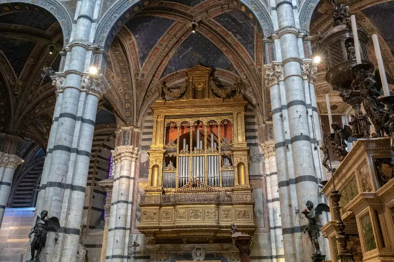 Buffet doré d'un grand orgue entre des colonnes rayées noir et blanc, sous des voûtes peintes