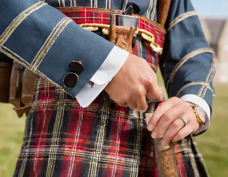 Tenue écossaise traditionnelle en gros plan : kilt en tartan rouge, veste bleue galonnée et dague à la ceinture